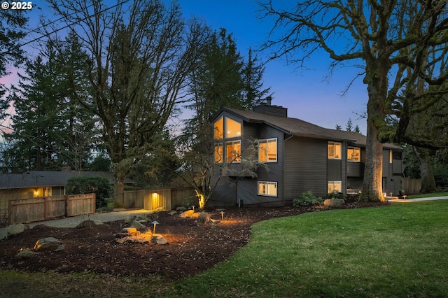 property exterior at dusk featuring a yard, a chimney, and fence