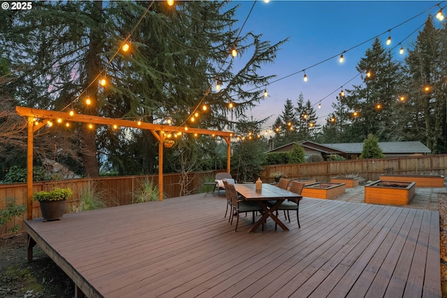 deck at dusk with a fenced backyard, a vegetable garden, and outdoor dining space