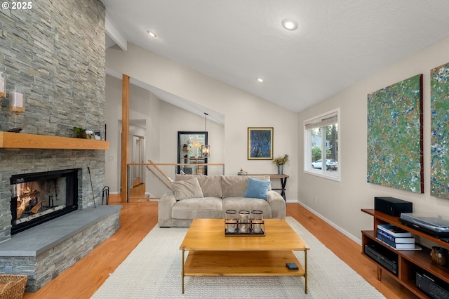 living room featuring lofted ceiling, baseboards, wood finished floors, and a stone fireplace