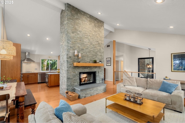 living room featuring vaulted ceiling with beams, light wood-style floors, recessed lighting, and a stone fireplace