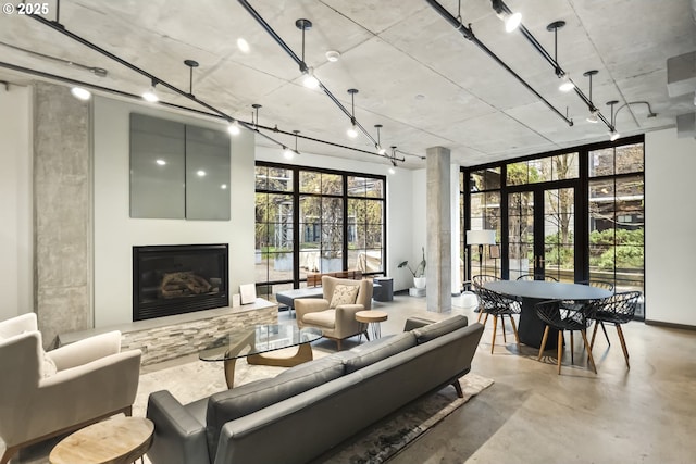 living area with a glass covered fireplace, rail lighting, concrete flooring, and french doors