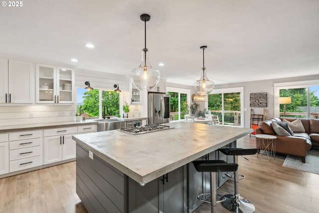 kitchen featuring a sink, appliances with stainless steel finishes, white cabinets, light wood finished floors, and open floor plan