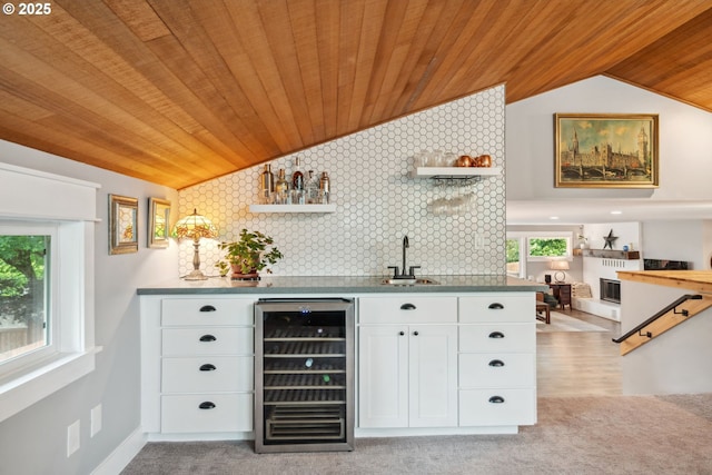 indoor wet bar featuring wine cooler, wooden ceiling, vaulted ceiling, a fireplace, and light carpet