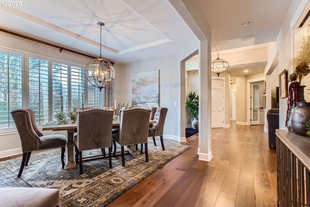 dining space with plenty of natural light, hardwood / wood-style floors, a raised ceiling, and a notable chandelier