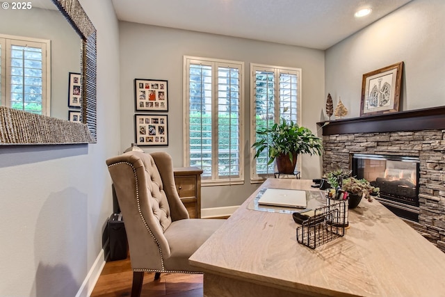 office area with hardwood / wood-style flooring, plenty of natural light, and a stone fireplace