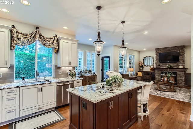 kitchen with sink, dark wood-type flooring, dishwasher, a kitchen island, and decorative light fixtures