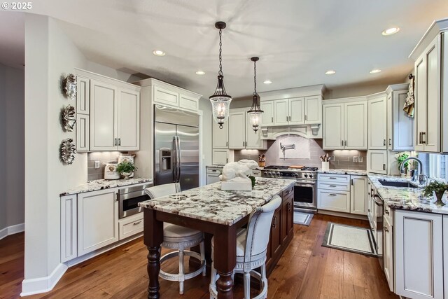 kitchen with light stone countertops, a center island, decorative light fixtures, dark hardwood / wood-style flooring, and built in appliances