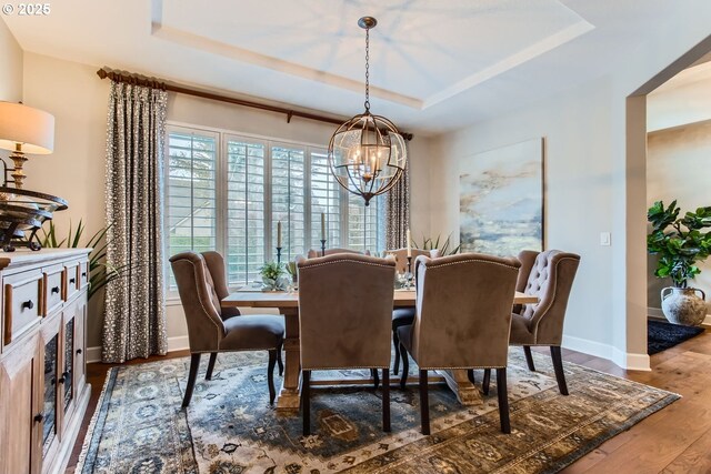 dining area with a raised ceiling, wood-type flooring, and an inviting chandelier