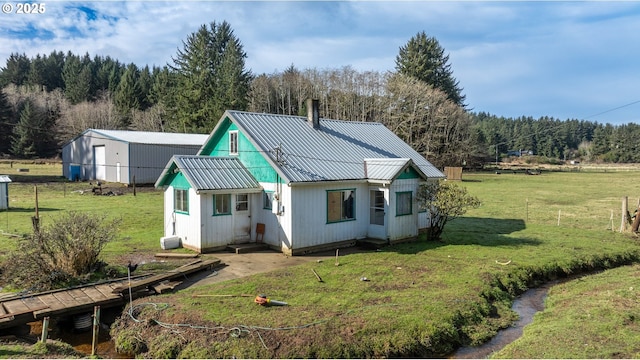 back of house with an outdoor structure, metal roof, a lawn, and a forest view