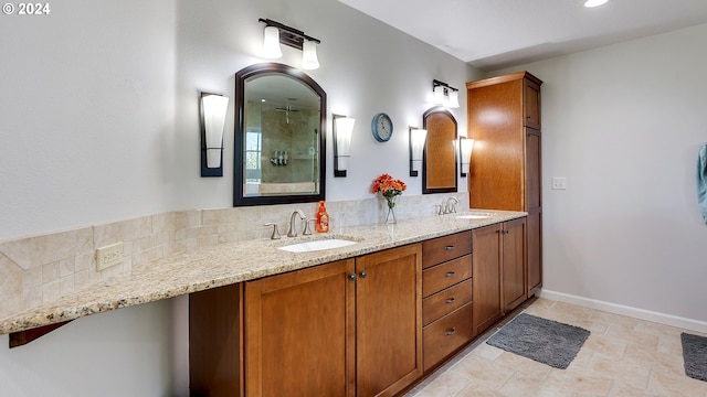 full bath with a sink, baseboards, a tile shower, and double vanity