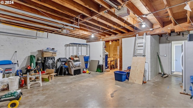 unfinished basement featuring concrete block wall and freestanding refrigerator