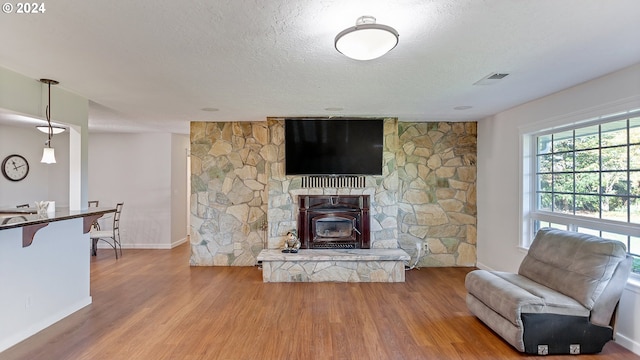 living room with a textured ceiling, a stone fireplace, visible vents, wood finished floors, and baseboards