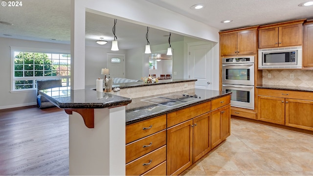 kitchen with a textured ceiling, brown cabinets, dark stone countertops, backsplash, and stainless steel appliances