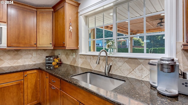 kitchen with a sink, plenty of natural light, brown cabinets, and dark stone countertops