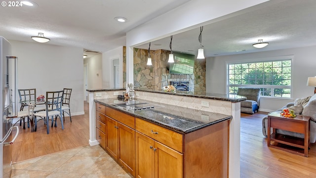 kitchen with a stone fireplace, brown cabinets, black electric cooktop, baseboards, and open floor plan