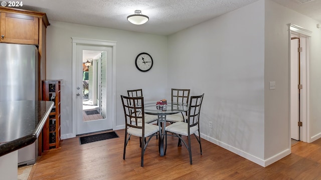 dining area featuring baseboards, light wood finished floors, a textured ceiling, and visible vents