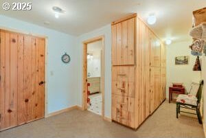 hall featuring light colored carpet and baseboards