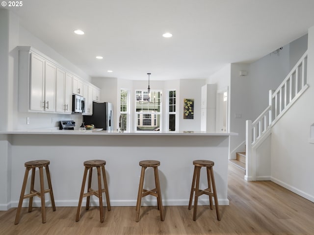7804 SW Brookline Ln, Portland, OR 97224 - kitchen with appliances with stainless steel finishes, light wood finished floors, a kitchen breakfast bar, light countertops, and recessed lighting
