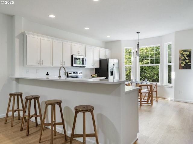 7804 SW Brookline Ln, Portland, OR 97224 - kitchen with appliances with stainless steel finishes, a peninsula, a breakfast bar, light countertops, and light wood-type flooring