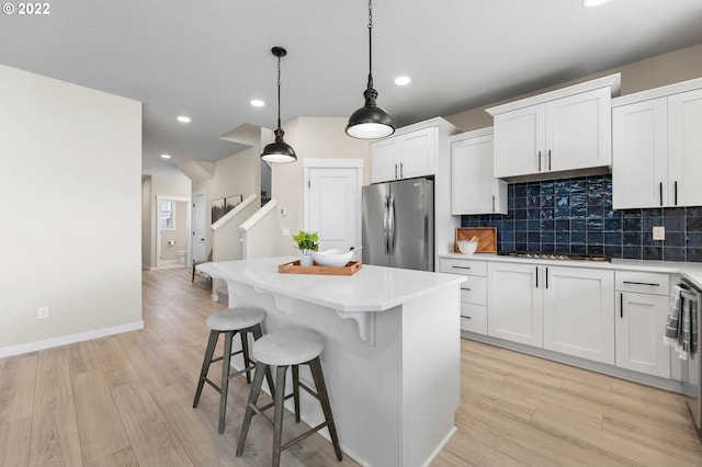 kitchen featuring a kitchen island, stainless steel refrigerator, white cabinetry, hanging light fixtures, and light hardwood / wood-style flooring