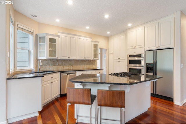 kitchen with a kitchen breakfast bar, stainless steel appliances, a center island, sink, and white cabinetry