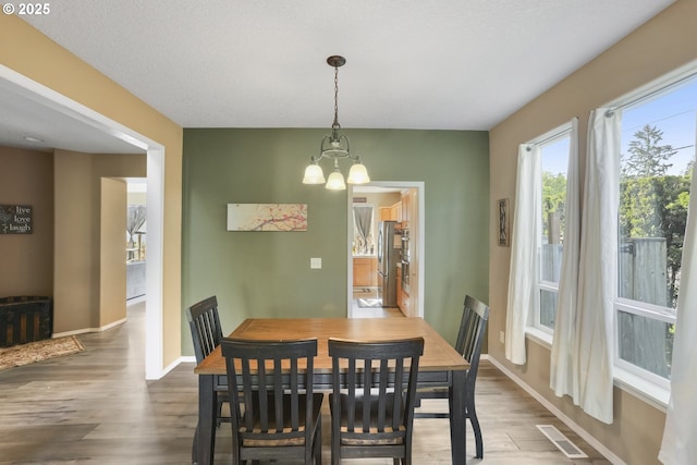 dining room featuring an inviting chandelier, baseboards, wood finished floors, and visible vents