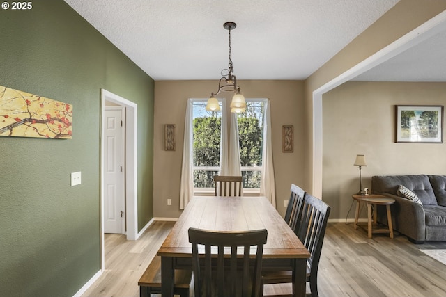 dining room featuring an inviting chandelier, light wood finished floors, a textured wall, and baseboards
