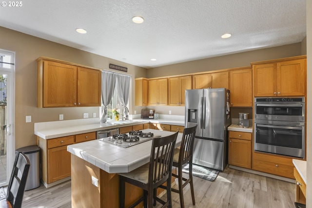 kitchen featuring appliances with stainless steel finishes, a sink, light wood-style floors, tile counters, and a center island