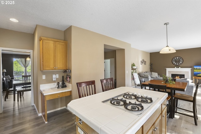 kitchen with wood finished floors, open floor plan, tile counters, white gas stovetop, and a tiled fireplace