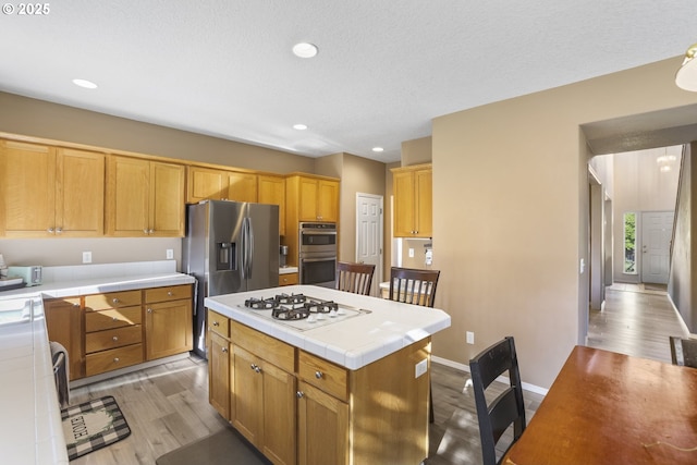 kitchen with appliances with stainless steel finishes, tile counters, baseboards, light wood-type flooring, and a kitchen island