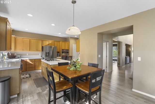 kitchen with a sink, stainless steel fridge with ice dispenser, baseboards, light wood finished floors, and tile counters