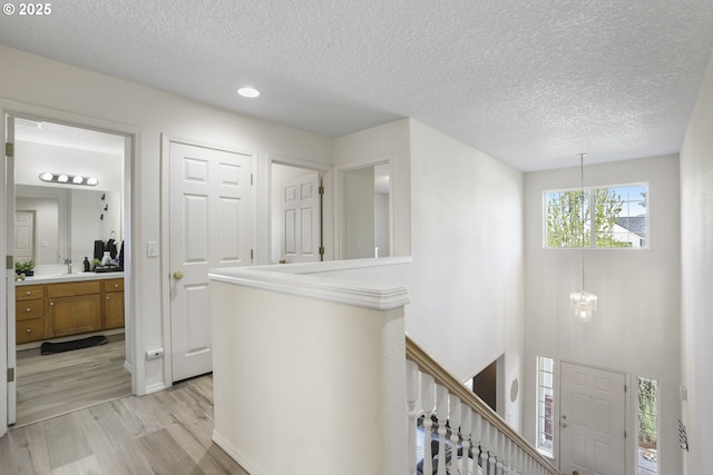 corridor with a textured ceiling, a chandelier, recessed lighting, an upstairs landing, and light wood-type flooring