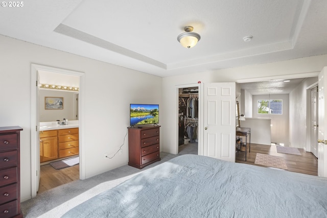 bedroom with light colored carpet, a closet, a spacious closet, a tray ceiling, and ensuite bath