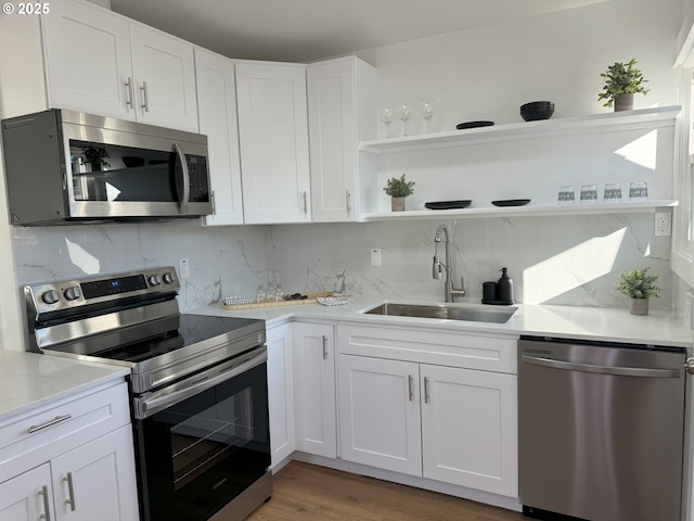 kitchen featuring appliances with stainless steel finishes, a sink, decorative backsplash, and open shelves