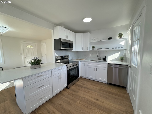 kitchen with wood finished floors, stainless steel appliances, white cabinetry, open shelves, and a sink