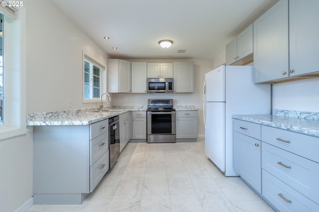 kitchen with gray cabinetry, light stone counters, appliances with stainless steel finishes, marble finish floor, and a sink