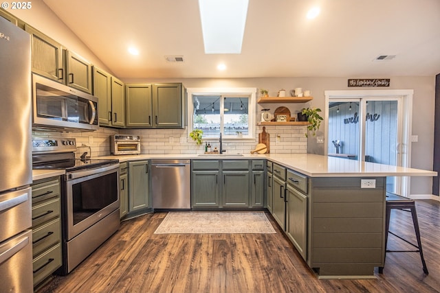 kitchen featuring a kitchen breakfast bar, a peninsula, visible vents, appliances with stainless steel finishes, and a sink