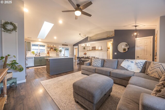 living area with dark wood-style flooring, ceiling fan with notable chandelier, and lofted ceiling with skylight