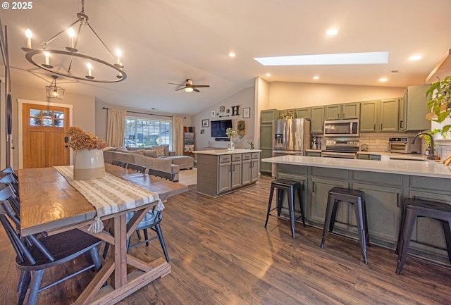 dining space featuring vaulted ceiling with skylight, ceiling fan with notable chandelier, dark wood-type flooring, recessed lighting, and a toaster