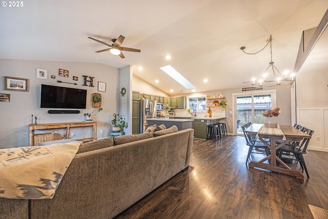 living area featuring ceiling fan with notable chandelier, dark wood-style flooring, wainscoting, and lofted ceiling