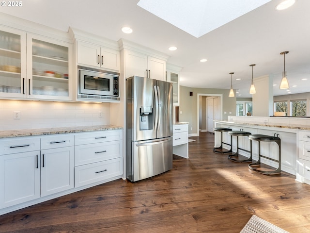 kitchen with white cabinetry, decorative light fixtures, stainless steel appliances, light stone countertops, and decorative backsplash