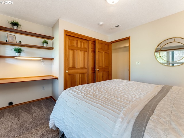 carpeted bedroom with a closet, built in desk, and a textured ceiling