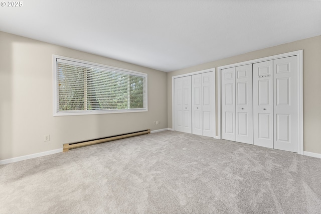 unfurnished bedroom with baseboard heating, multiple closets, and light colored carpet