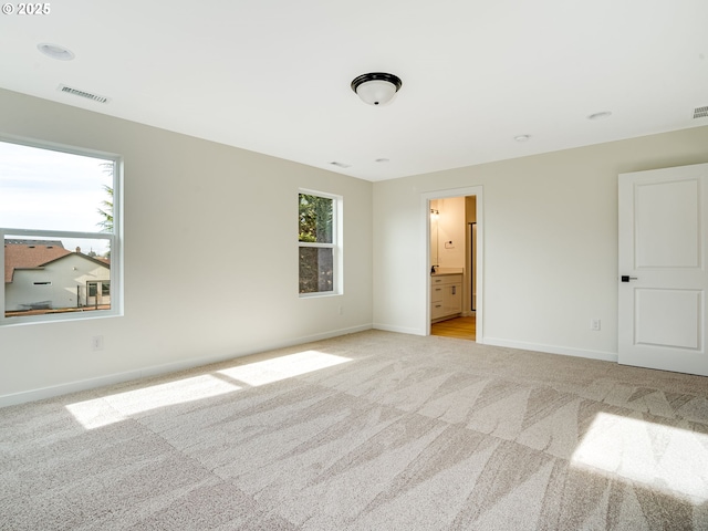 unfurnished bedroom featuring light carpet and ensuite bath