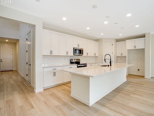 kitchen featuring light hardwood / wood-style flooring, stainless steel appliances, white cabinets, and a center island with sink