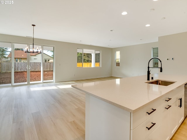 kitchen with white cabinetry, sink, hanging light fixtures, a kitchen island with sink, and light hardwood / wood-style flooring