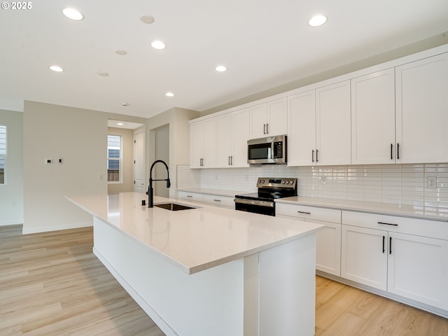 kitchen with sink, light hardwood / wood-style flooring, appliances with stainless steel finishes, white cabinetry, and a center island with sink