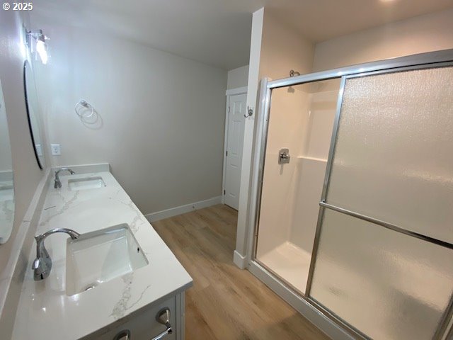 full bathroom featuring double vanity, wood finished floors, a shower stall, and baseboards