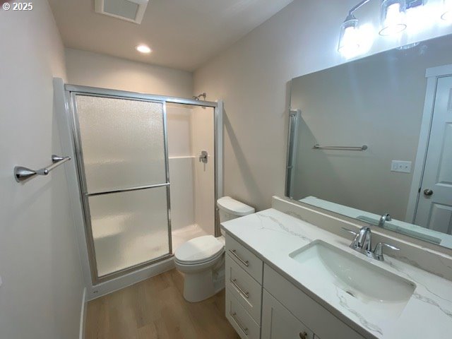 bathroom with wood finished floors, a stall shower, toilet, vanity, and recessed lighting