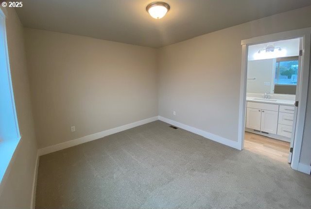 empty room with a sink, light carpet, and baseboards